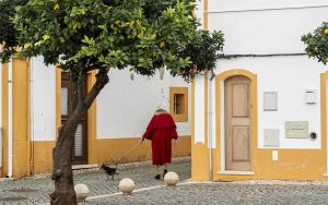 Lady wearing a capote, a traditional Alentejo coat, and walking her small dog in Vila Viscoça.