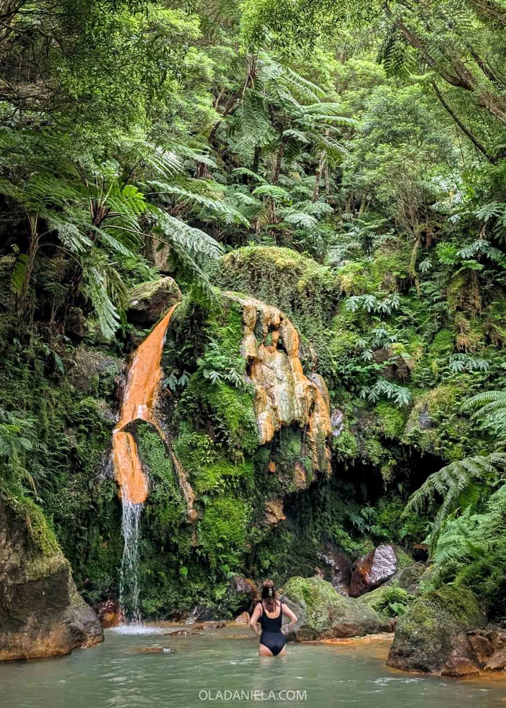 Daniela in a black swimsuit walking toward the hot waterfall at Caldeira Velha on São Miguel Island, Azores