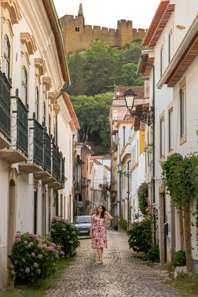 A woman walking down a street in Tomar with the castle looming above
