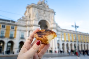 Holding a pastel de nata in front of the Rua Augusto Arch